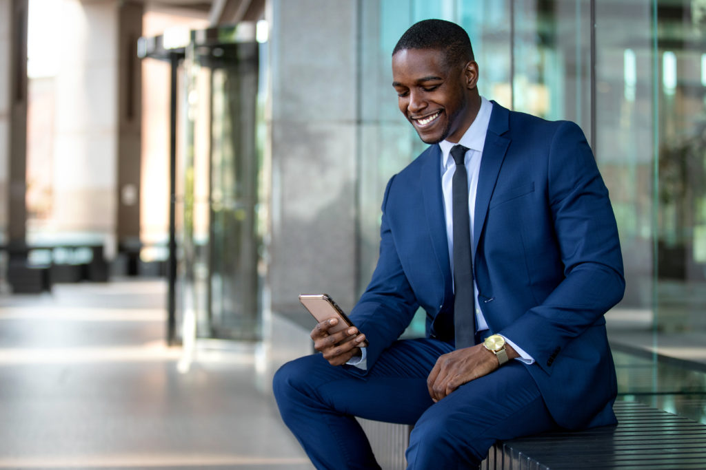 A young black businessman wearing a suit checks his employee benefits on the HFH Go app on his phone.