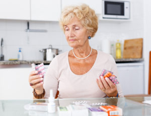A senior woman holds multiple packs of prescribed medication having difficulty with medication management.