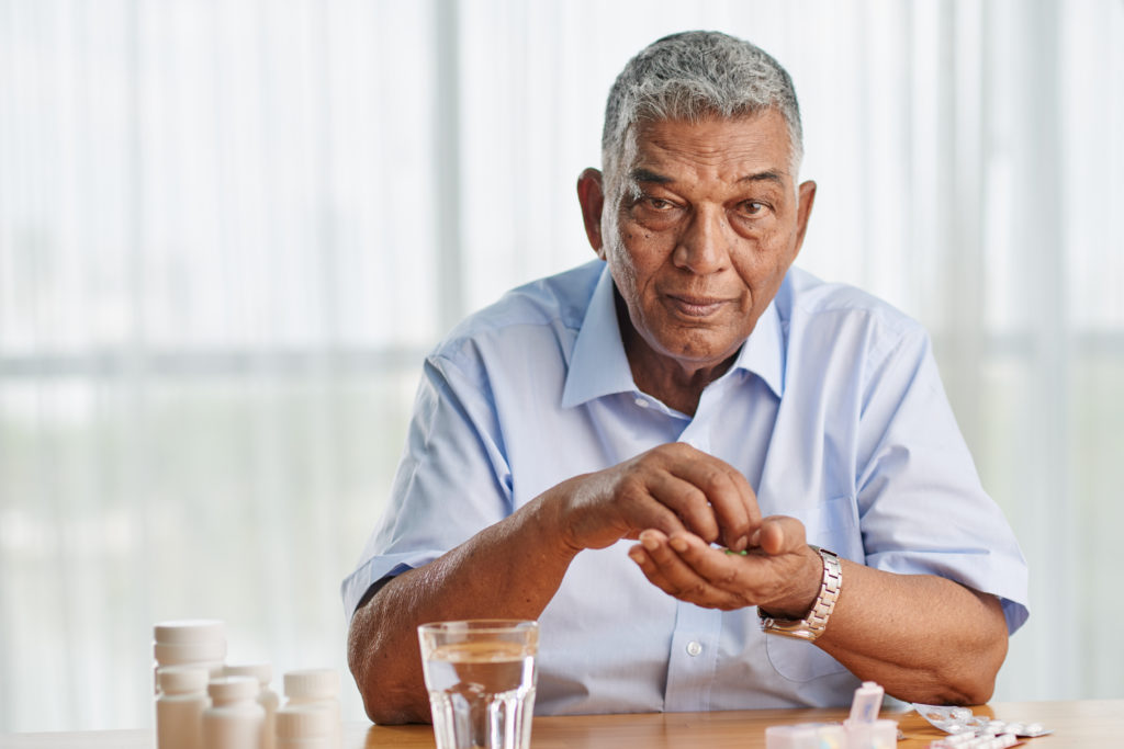A male senior in a blue shirt gets ready to take daily prescribed medication as part of his medication management. 