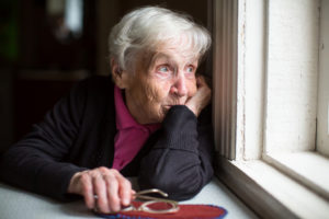 Older woman look sadly out of her window.