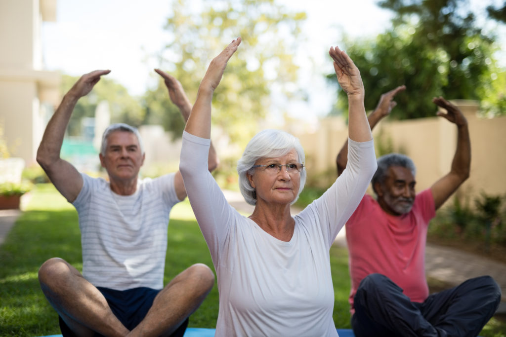 Senior residents stretching for physical exercise with hands raised while sitting in a park