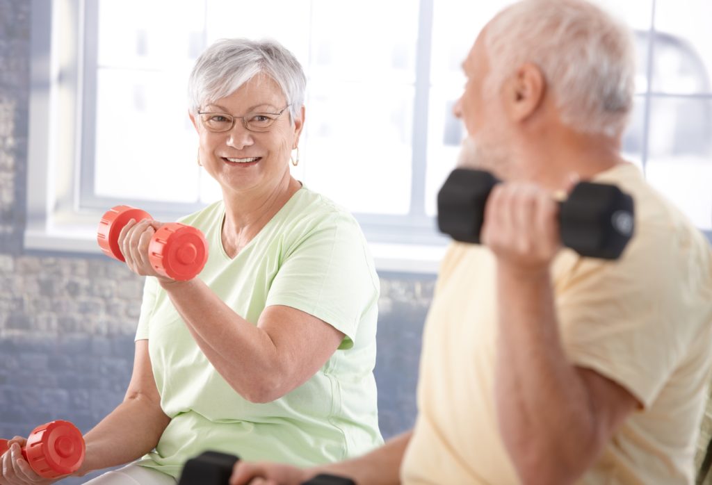 Active seniors smile while they lift weights.