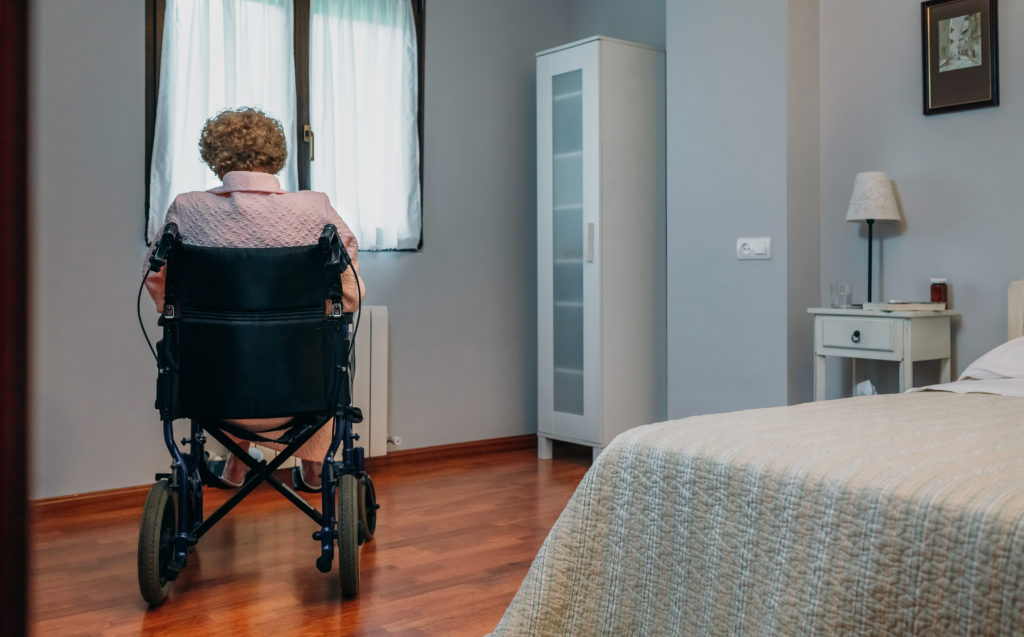 Senior woman in a wheelchair alone in her room looking out of a window.