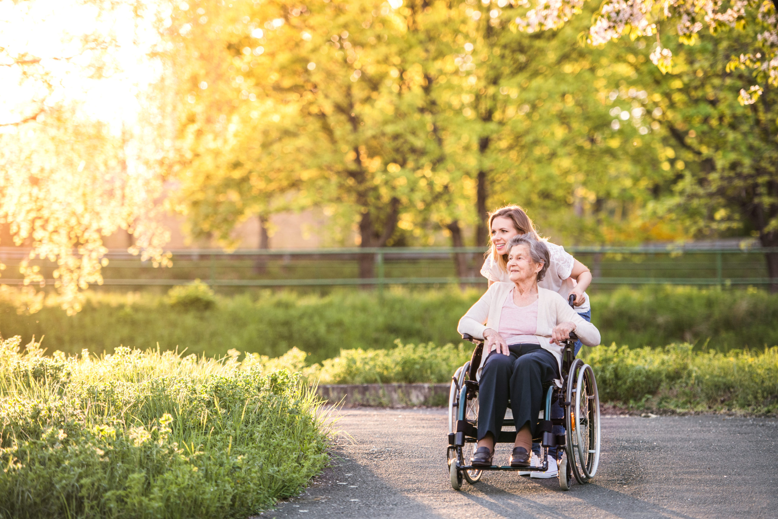 Woman pushing her mother in a wheelchair along an outdoor path.