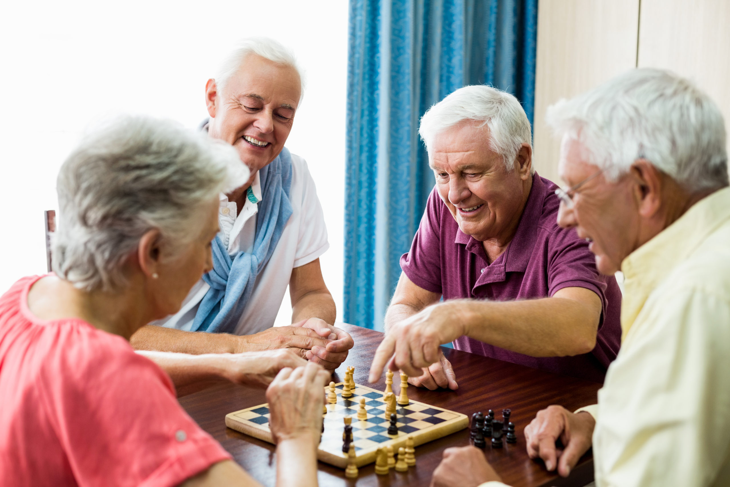 Group of seniors is playing chess and smiling as they have fun together. 
