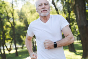 Older man wears a smart watch while jogging in the park. 