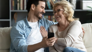 Son and mother smile and laugh while looking at a smart phone. 