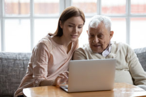 A daughter and her aged father use a laptop computer together.