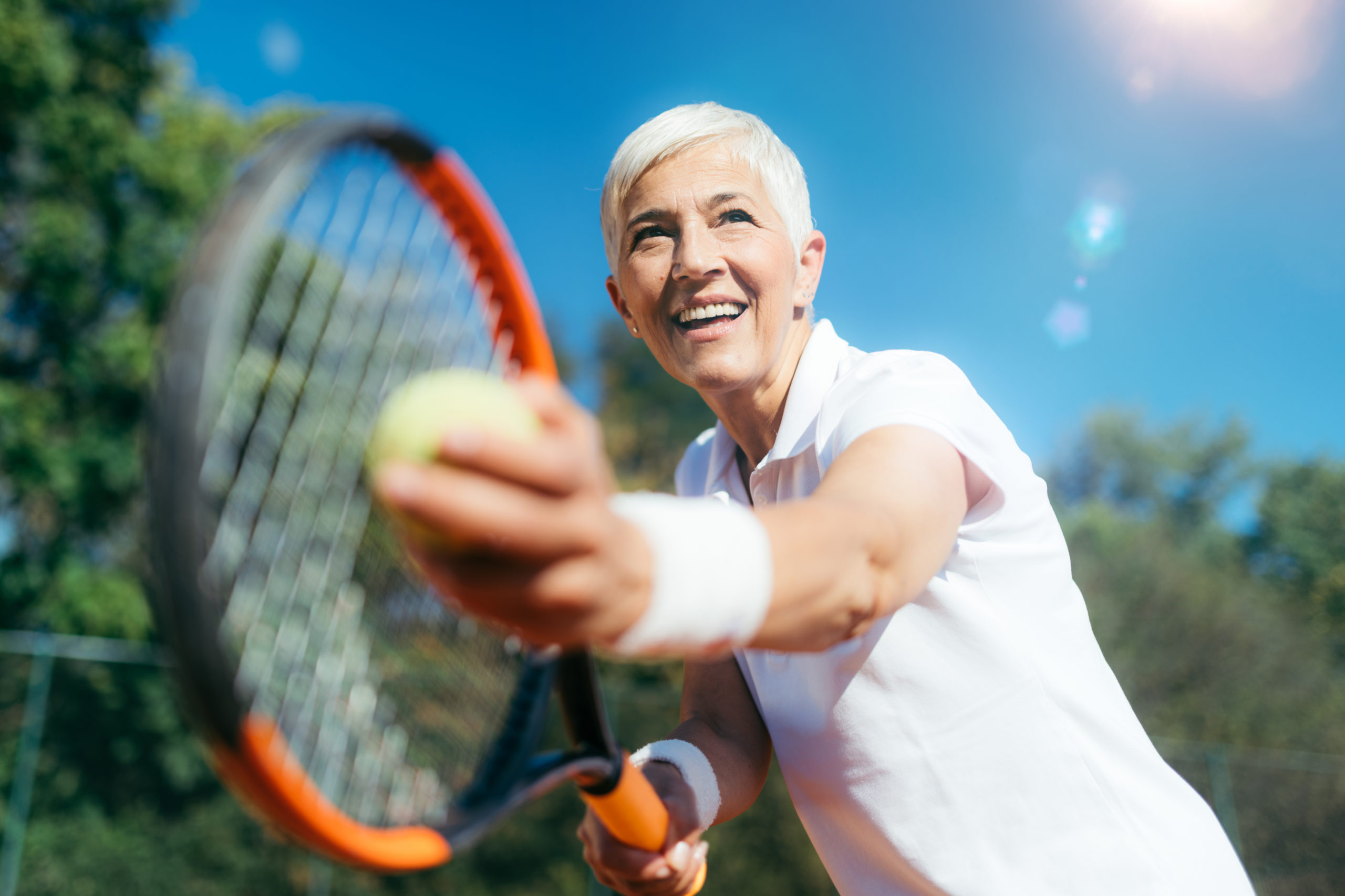 Elderly woman playing tennis and smiling.