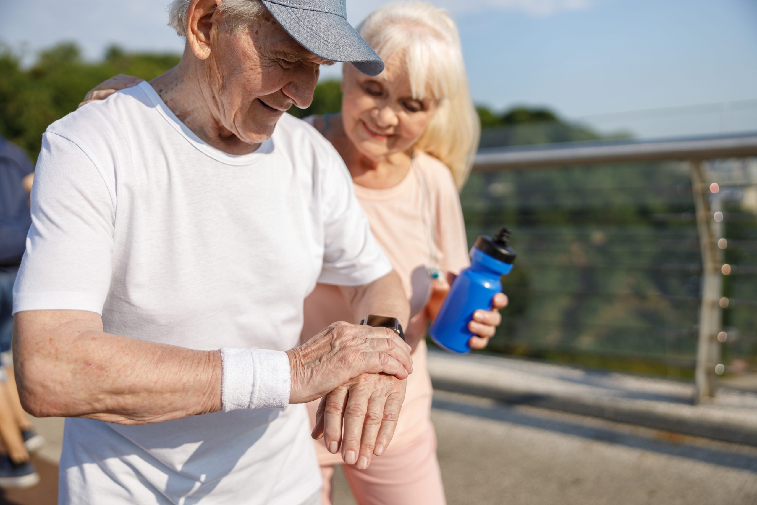 Active seniors check heart rate on a medical alert smartwatch during an outdoor walk. 