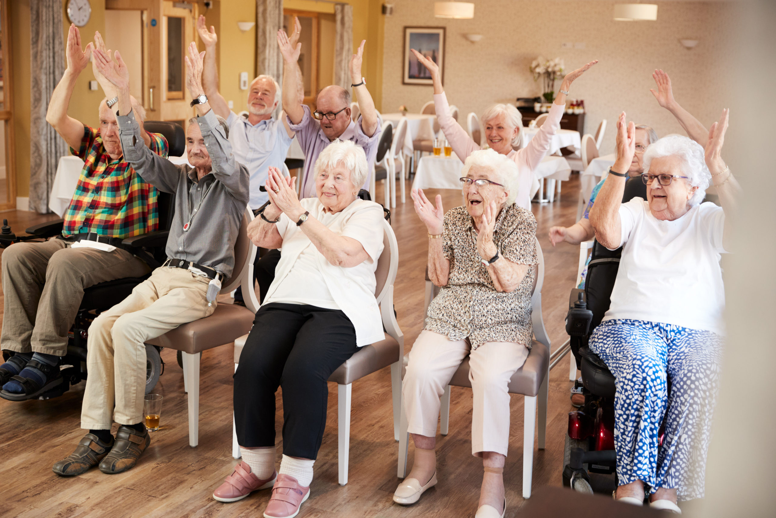 Group of happy seniors sits with their hands in the air at their nursing home.