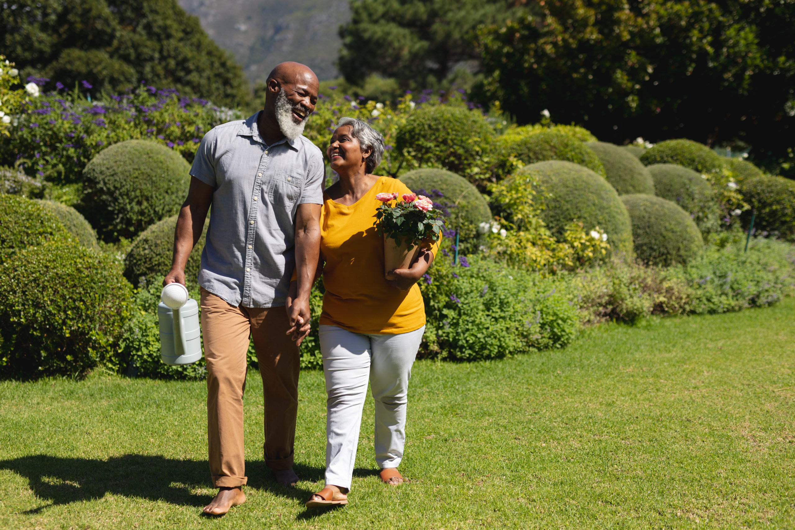 A senior couple walks through a garden while holding hands. 