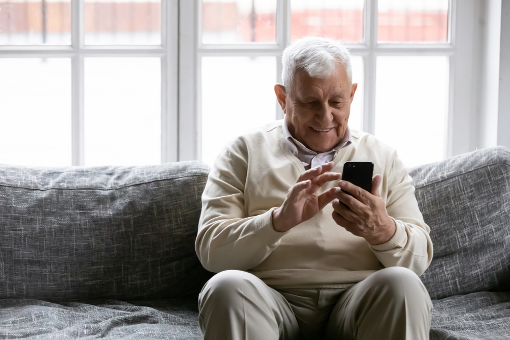  Senior man on a couch using his phone and smiling. 
