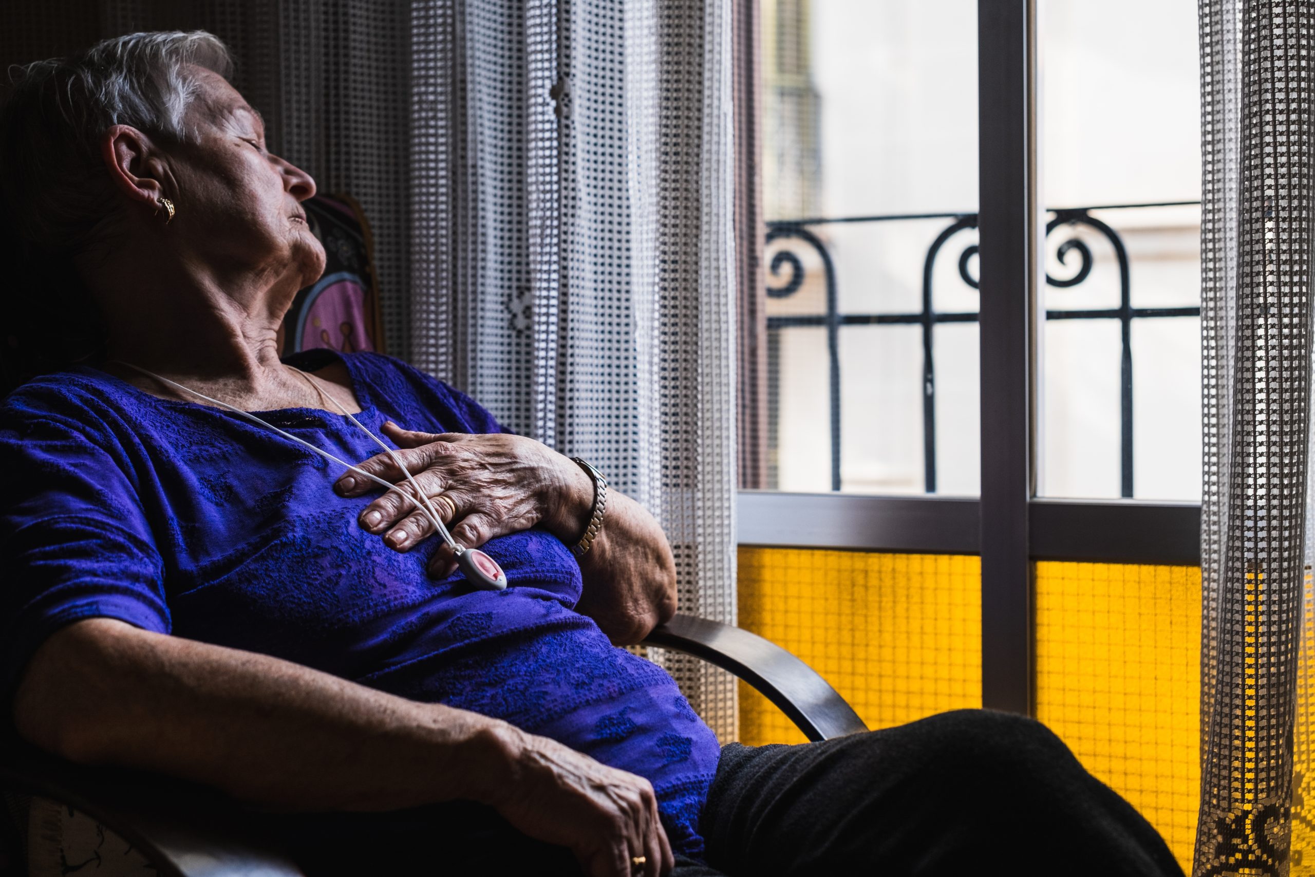 A senior woman naps with her emergency pendant around her neck. 