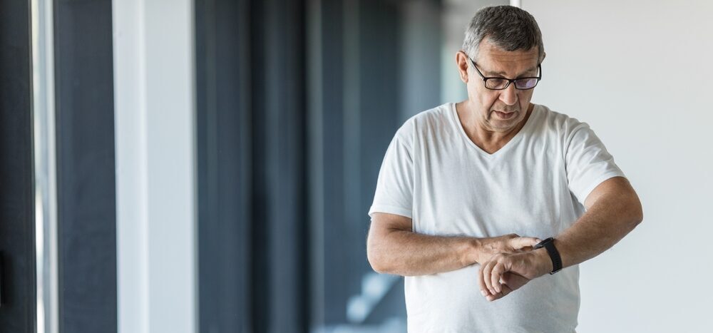 While exercising, a senior man checks his medical alert watch for his heart rate.
