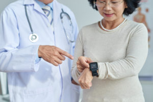 A doctor instructs a senior woman on how to use her medical alert watch.