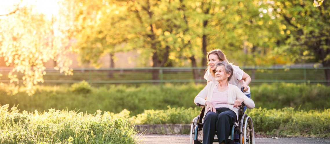 Woman pushing her mother in a wheelchair along an outdoor path.