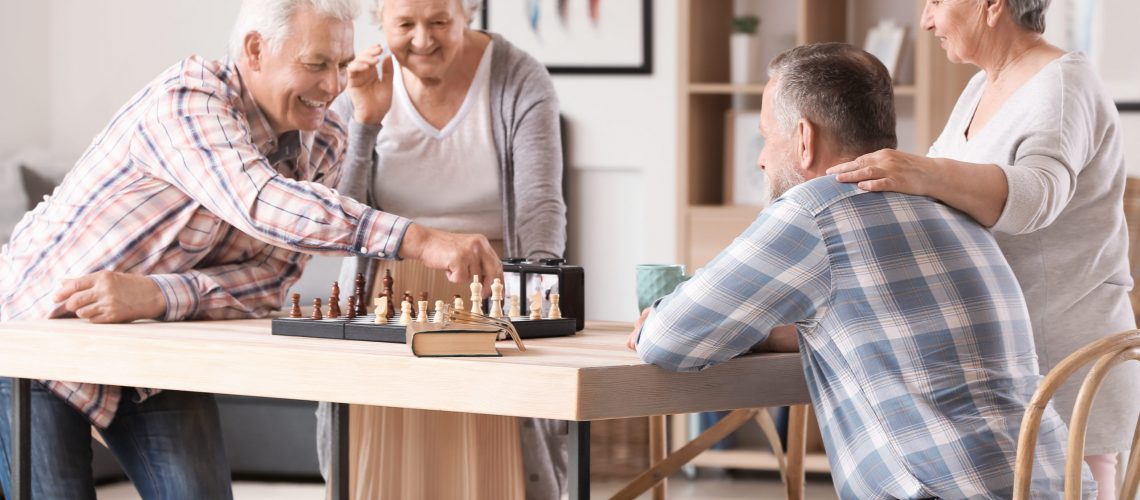 Happy seniors play chess together in the game area of a senior living community.