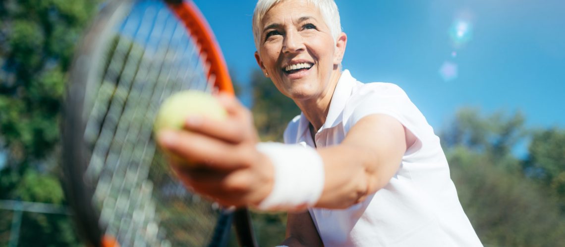 Elderly woman playing tennis and smiling.