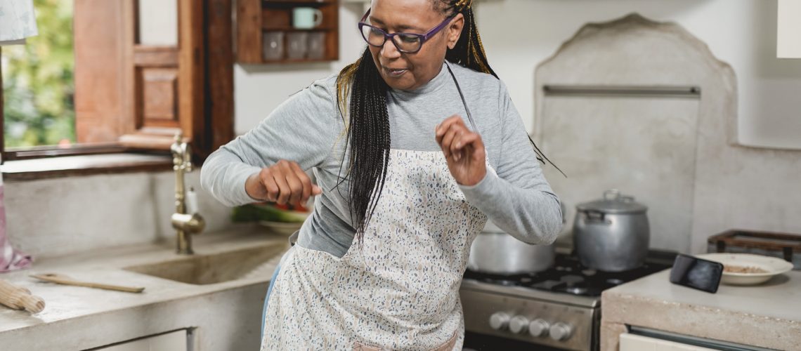 Senior woman dancing in her kitchen while preparing a meal.