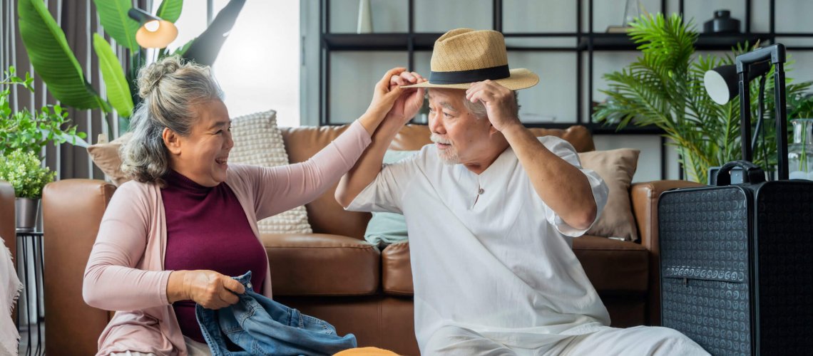 An older Asian couple sitting in living room and pack a suitcase together.