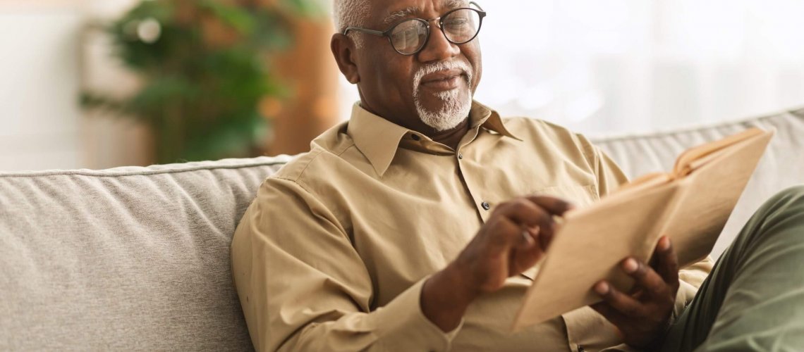 Senior man sitting on the couch reading a book.