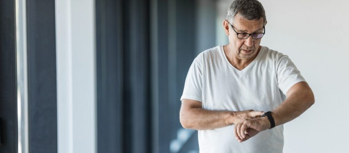 While exercising, a senior man checks his medical alert watch for his heart rate.