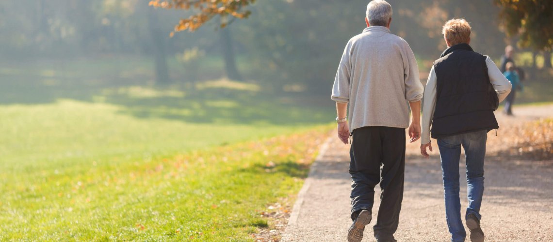 Two seniors walking outside on a trail.