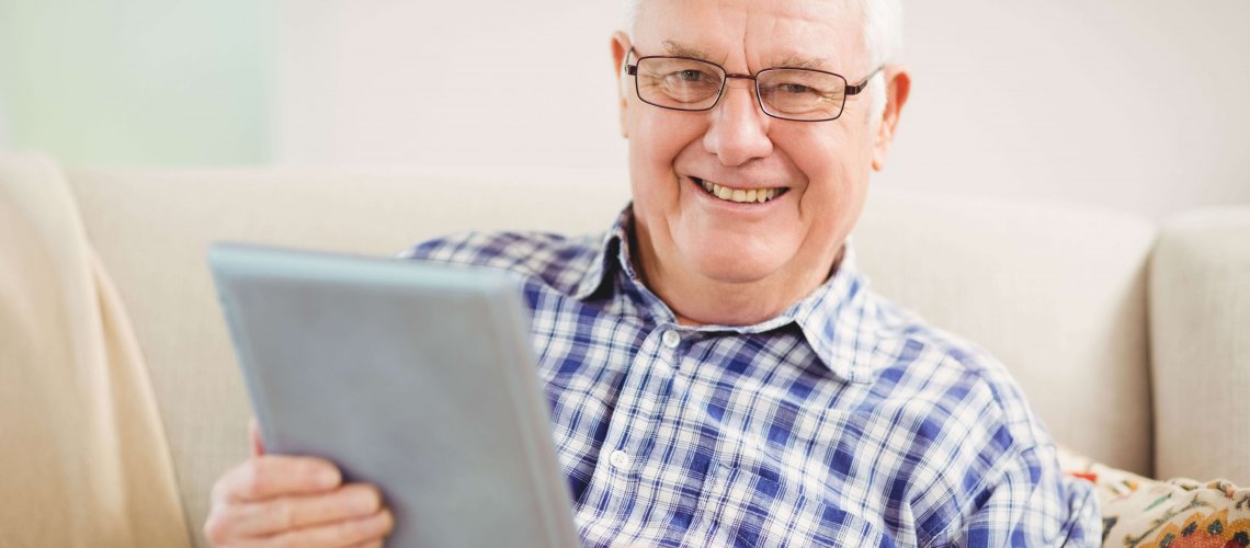 Senior man smiling and using a tablet.