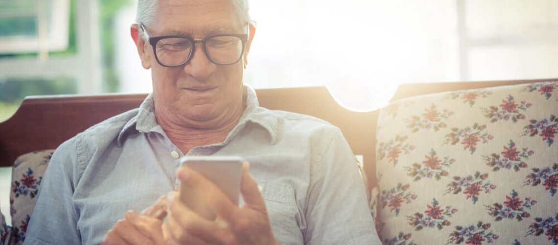 Senior sitting on a couch using his phone.