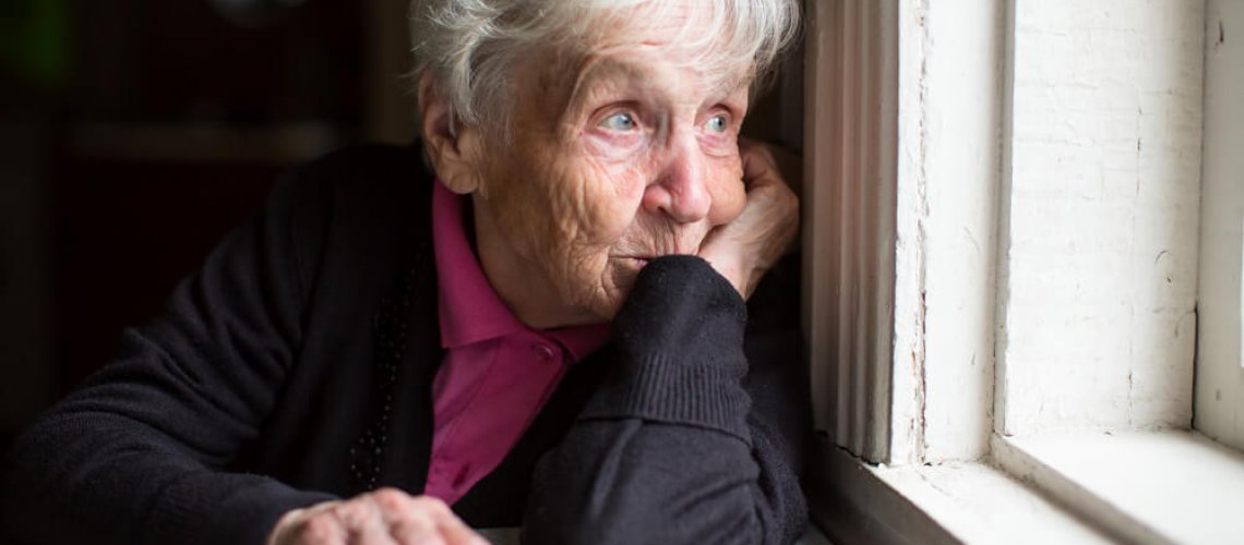 Older woman look sadly out of her window.