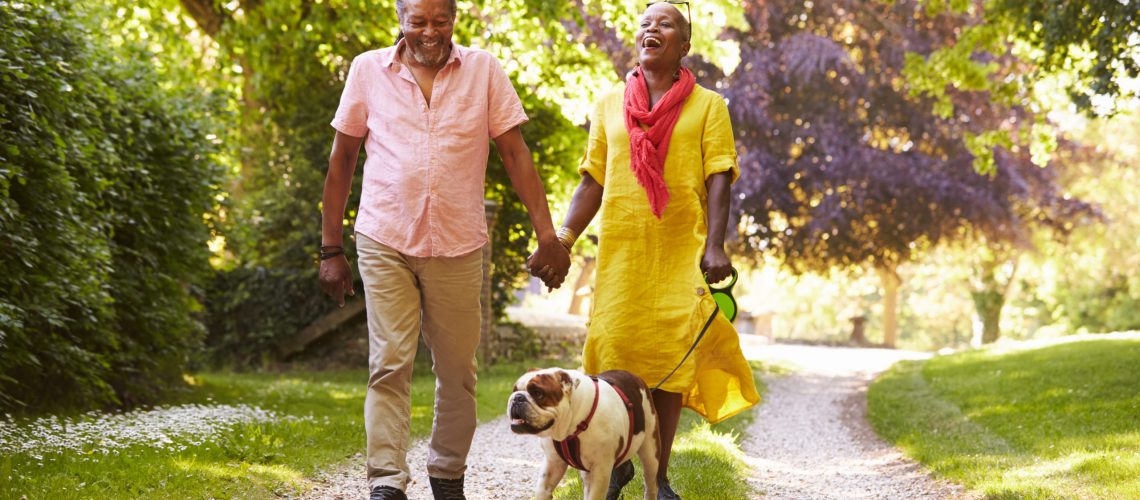 Happy senior couple wearing smartwatches walks their dog outdoors.