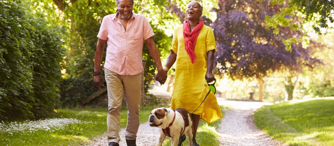 Happy senior couple wearing smartwatches walks their dog outdoors.