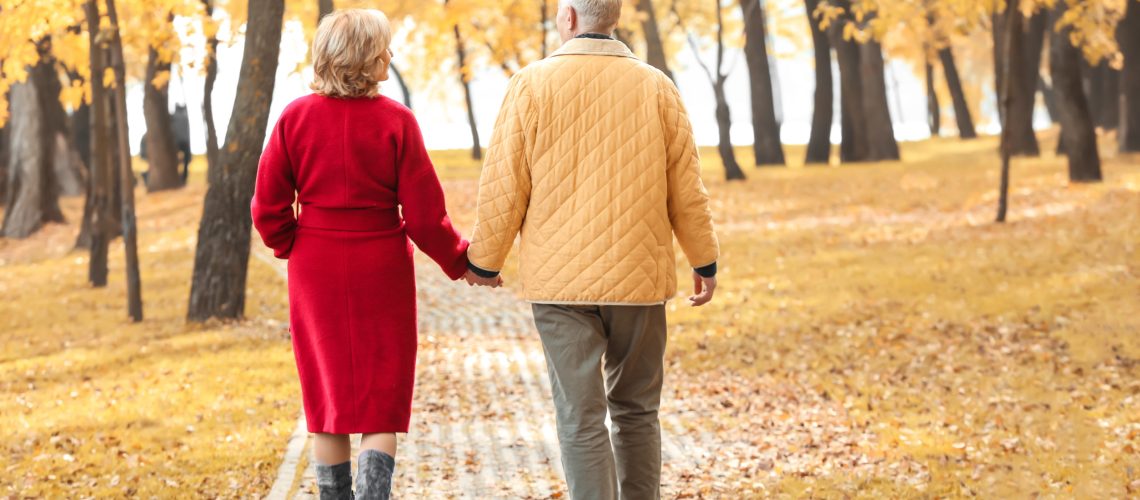 Older couple walks through the park with fall foliage around them.